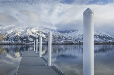 Säulen am Steg eines Sees in der Nähe einer schneebedeckten Bergkette - MINF15204