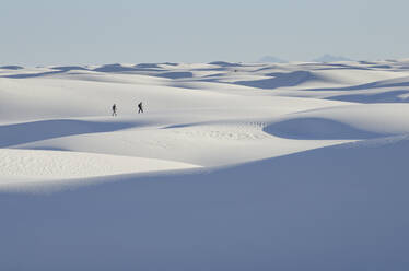 Two people at a distance walking across white sand dunes. - MINF15205