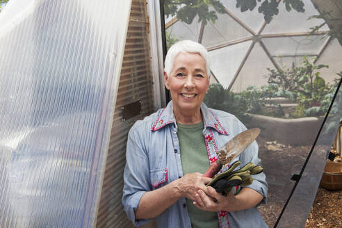 Smiling senior woman gardening in a geodesic dome, climate controlled glass house - MINF15208