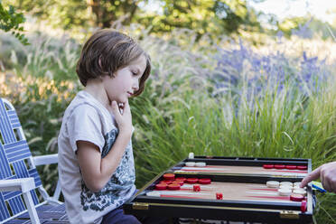 Ein kleiner Junge spielt Backgammon in einem Garten. - MINF15235