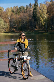 Frau mit Fahrrad auf dem Steg über dem See an einem sonnigen Tag - KNTF05741