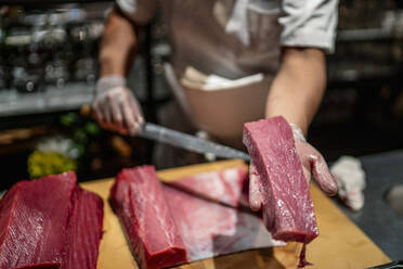 Männlicher Koch zeigt ein Stück rohe Meeresfrüchte in der Küche eines Restaurants - OCMF01748