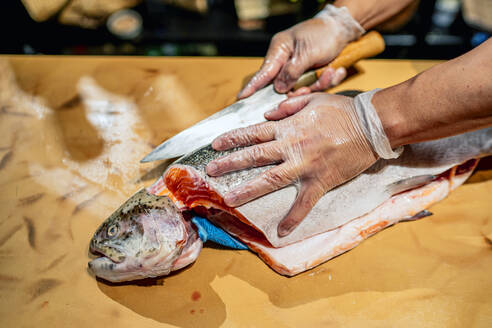 Männlicher Koch schneidet Fisch am Tresen eines Restaurants - OCMF01753