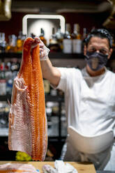 Männlicher Chefkoch zeigt großen rohen Fisch in der Küche eines Restaurants - OCMF01754