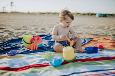 Kleiner Junge spielt mit Spielzeug am Strand bei Sonnenuntergang - GMLF00725