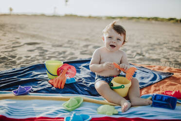 Happy male toddler looking away while playing at beach - GMLF00728