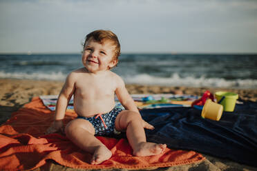 Süßes Baby lächelnd am Strand sitzend an einem sonnigen Tag - GMLF00729