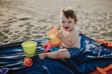 Cheerful cute baby boy playing at beach during sunset on sunny day - GMLF00731