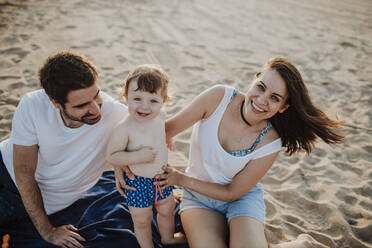 Smiling family with baby boy at beach during sunset - GMLF00735