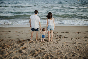 Mann und Frau mit Sohn betrachten die Aussicht, während sie bei Sonnenuntergang am Strand stehen - GMLF00738