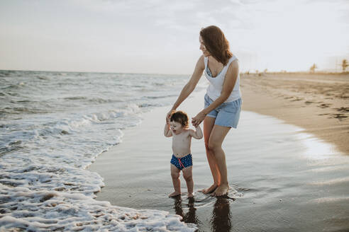 Mother and son enjoying in water at beach during sunset - GMLF00741