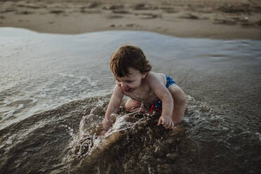 Kleiner Junge spielt im Wasser am Strand bei Sonnenuntergang - GMLF00751