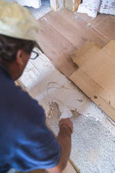 Männlicher Arbeiter beim Verlegen von Zement auf einem Parkettboden in einem Haus - SNF00680