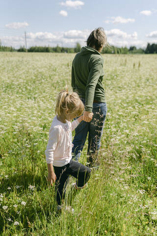 Mother holding hand of daughter while walking on meadow stock photo