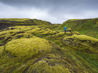 Man exploring green landscape against cloudy sky - LAF02489