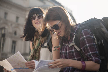 Women on vacation reading map while sitting at town square - AJOF00272
