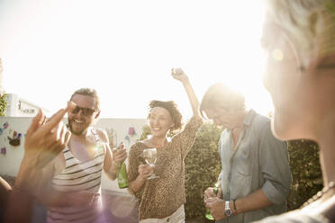 Happy male and female friends enjoying dancing at pool party against sky during sunset - AJOF00295