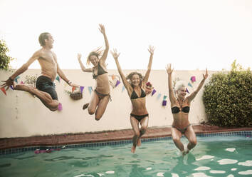 Carefree friends jumping together into swimming pool against sky during sunset - AJOF00298