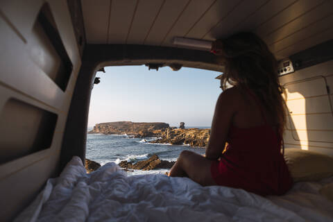 Woman admiring sea view while sitting in camper van at beach stock photo