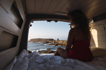 Woman admiring sea view while sitting in camper van at beach - DCRF00966