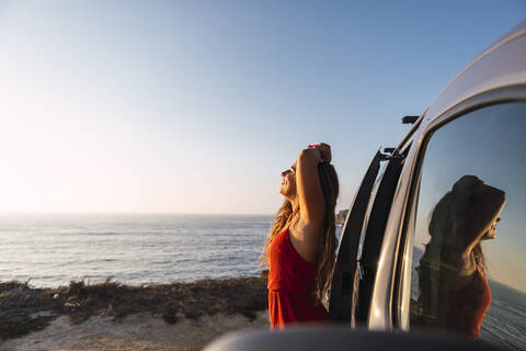 Smiling woman standing by camper van at beach stock photo