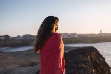 Junge Frau mit bedecktem Schal, die am Strand stehend die Aussicht betrachtet - DCRF00984