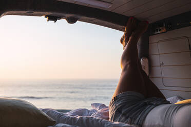 Woman relaxing while lying in camper van during sunset at beach - DCRF00994