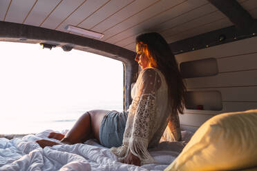 Frau im Wohnmobil sitzend bei Sonnenuntergang am Strand - DCRF00995