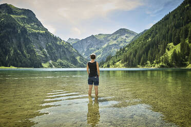 Ältere Frau steht knietief im Vilsalpsee und schaut auf eine Bergkette an einem sonnigen Tag - DIKF00530