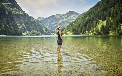 Mature woman standing knee deep in Vilsalpsee while listening music on sunny day - DIKF00531