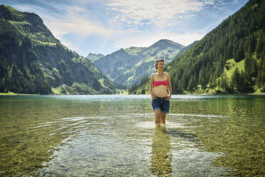 Reife Frau knietief im Vilsalpsee vor Bergkette an sonnigem Tag - DIKF00532