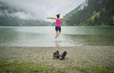 Aufgeregte Frau, die während der Regenzeit am Seeufer springt - DIKF00542