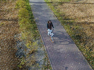 Frau fährt mit dem Fahrrad auf einem Fußweg in einem öffentlichen Park im Herbst - KNTF05763