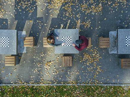 Boyfriend playing chess with girlfriend at table in park during autumn - KNTF05779