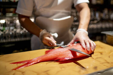 Koch schneidet Fisch auf einem Schneidebrett in einer Großküche eines Restaurants - OCMF01765