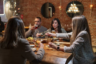 Friends having drink and food while sitting by table at restaurant - OCMF01772