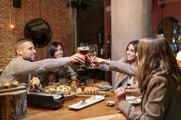 Lächelnde Freunde stoßen auf ein Getränk an, während sie am Tisch im Restaurant sitzen - OCMF01774