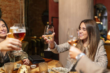 Friends toasting drink while sitting by table at restaurant - OCMF01775