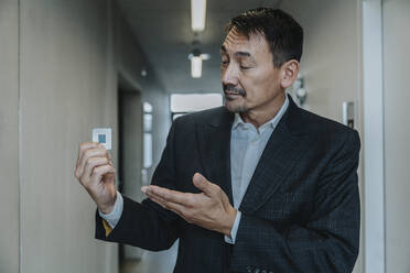 Business man showing computer chip while standing at clinic corridor - MFF06302