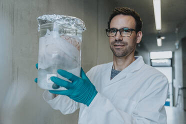 Scientist holding preserved human brain beaker while standing at clinic corridor - MFF06309