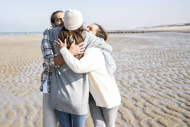 Young woman embracing man and mother while standing at beach - UUF21673