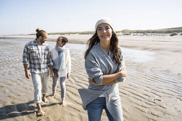 Young woman looking away while walking with family in background at beach - UUF21679