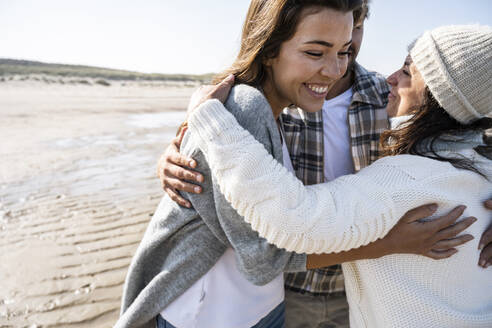 Reife Frau umarmt Paar, während sie am Strand steht - UUF21690