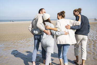 Family with arms around each other walking at beach - UUF21698