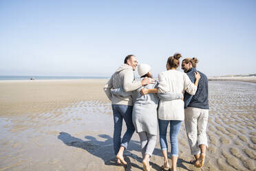 Family with arms around talking while walking together at beach - UUF21700
