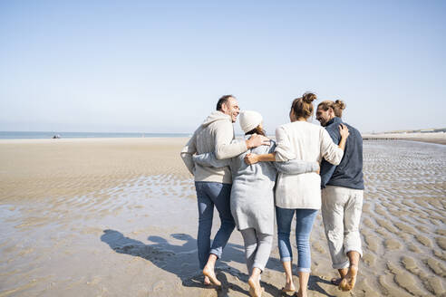 Familie, die sich beim gemeinsamen Strandspaziergang in den Armen liegt - UUF21700