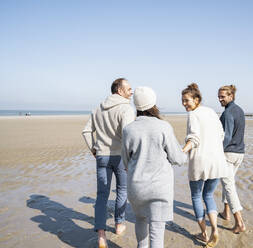 Smiling family holding hands of each other while walking at beach - UUF21701