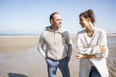 Smiling daughter and father talking while walking at beach - UUF21709