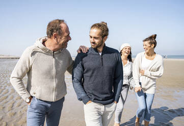 Männer unterhalten sich beim Gehen mit Frauen im Hintergrund am Strand - UUF21714