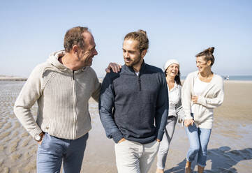 Men talking while walking with women in background at beach - UUF21714